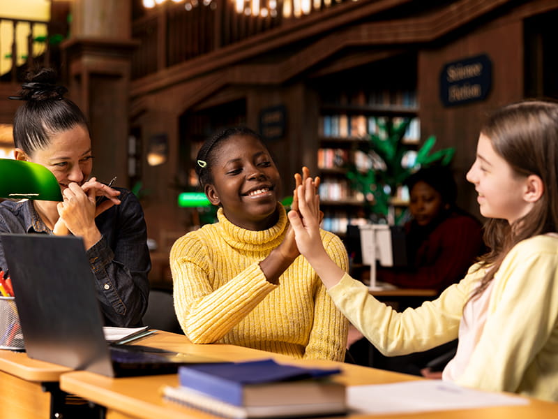 A black girl student giving a high five in a school library to a fellow student