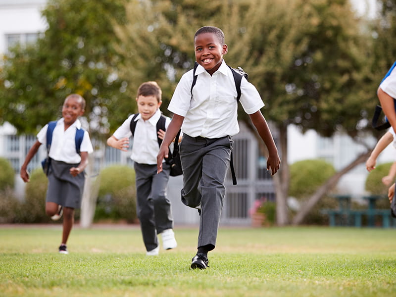 A group of international school children running across a school playing field